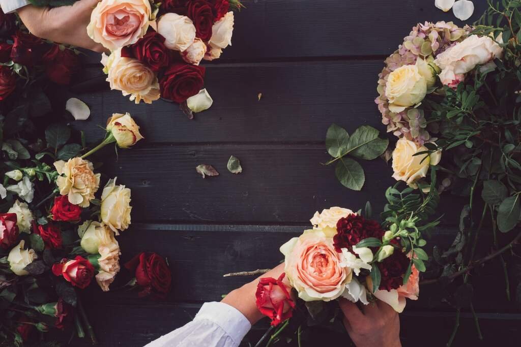 Seen from above: hands working loose roses into two bouquets on a dark wooden bench