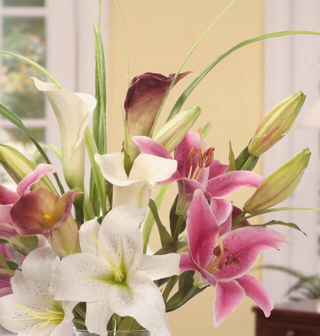 Pink and white lilies with a calla lily, standing tall in a clear vase