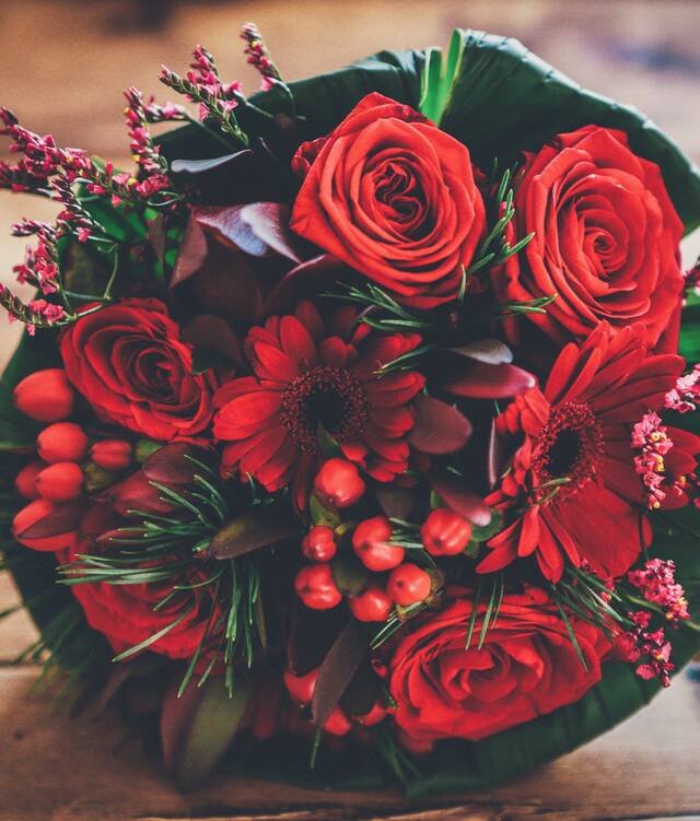 A round bouquet of red roses with red berries and heather