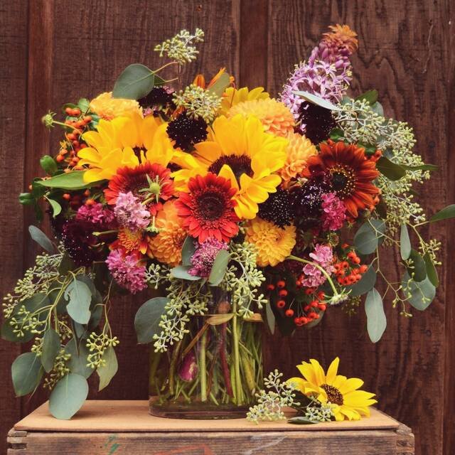 A big arrangement of sunflowers, dahlias and eucalyptus in a glass jar on a wooden crate