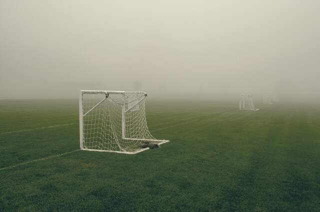 A goal on an empty playing field in thick morning fog.