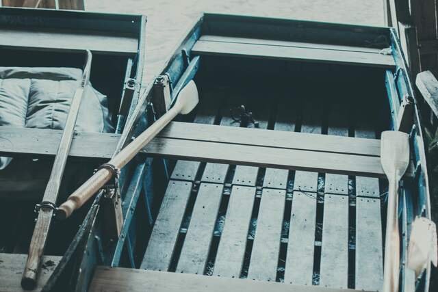 A wooden rowing boat back in the boathouse, its plain oars shipped across the thwarts.