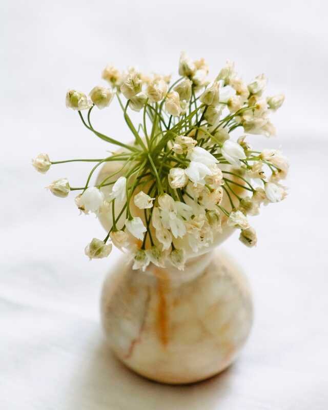 A small marble bud vase of white flowers on a linen tablecloth.