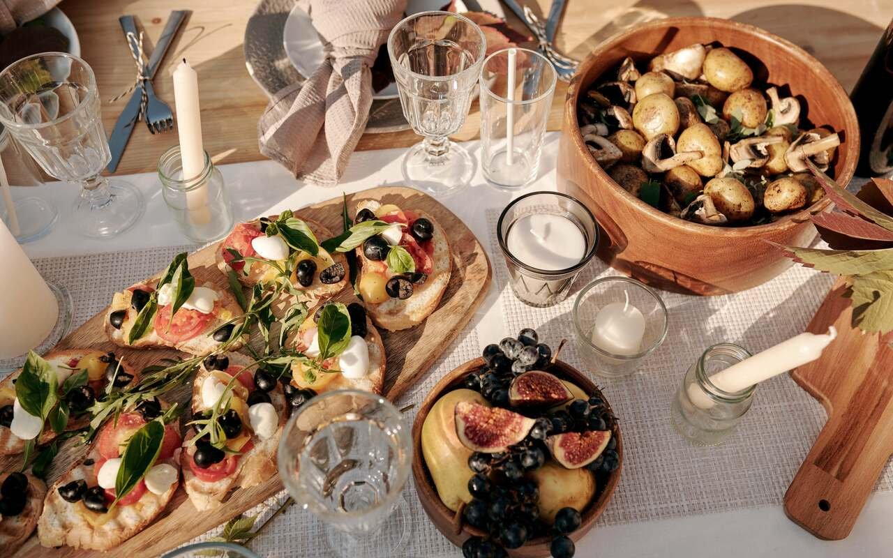 Tomato and soft cheese toasts on a wooden board, a bowl of figs and grapes, glasses catching the low sun.