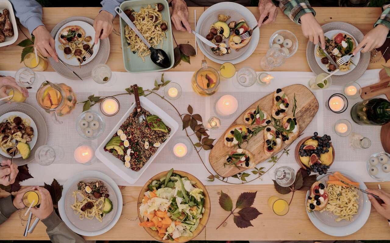 The whole table from above as the light goes: plates half eaten, grains with pomegranate, a bowl of leaves, candles burning down the middle.