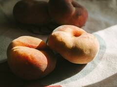 Ripe flat peaches in a slant of sun on a cloth.