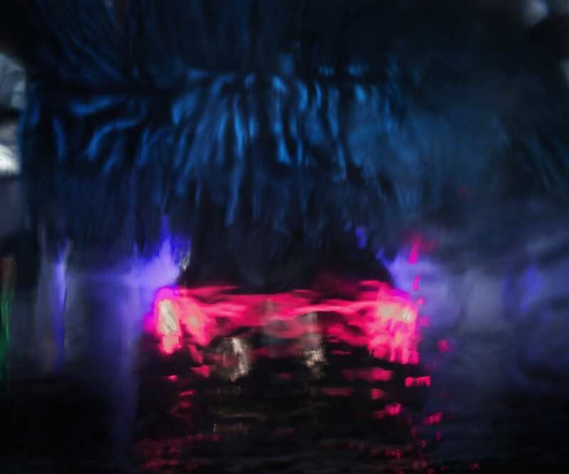 Soft foam washer curtains sweep the tunnel in blue light, the car's tail lamps glowing red through them.