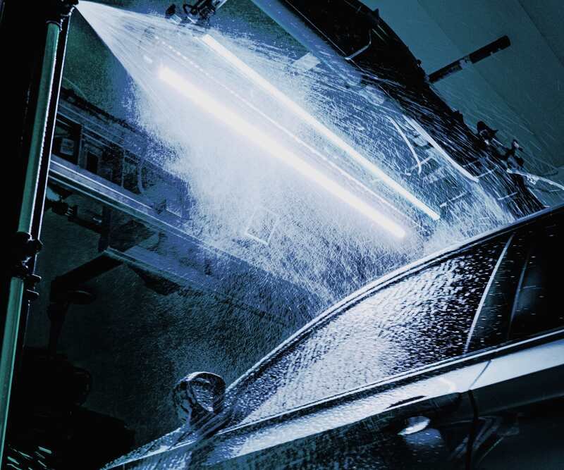 A spray bar lights up the arch above the car, mist falling across the windows and the door mirror.