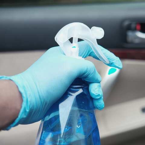 A gloved hand with a spray bottle, cleaning the inside of a car door.