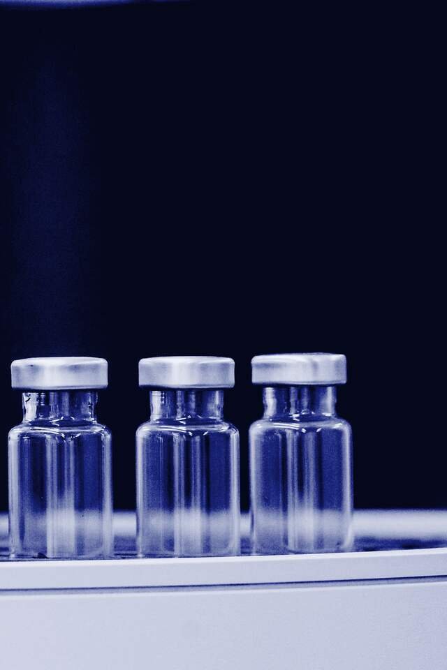 Stoppered glass vials on the inspection turntable, lit against the dark panel of the line.