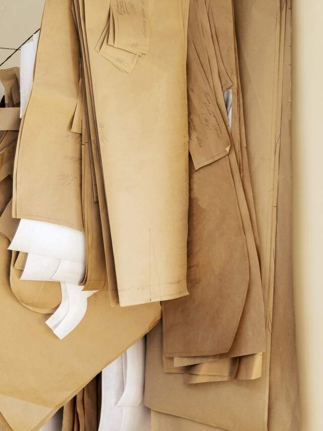 Brown paper patterns hanging from a rail, each bundle a client’s coat.