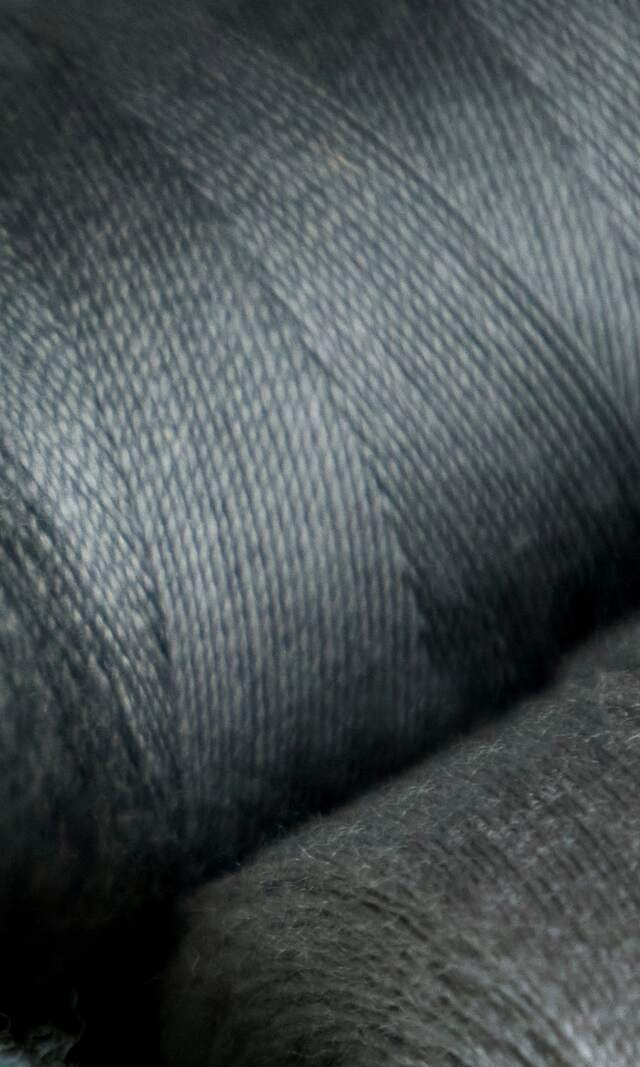 A spool of charcoal sewing thread, close enough to see each winding cross the last.