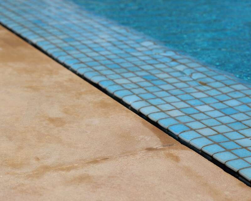 A pool deck stained rust-brown meeting a line of blue mosaic tile at the waterline.