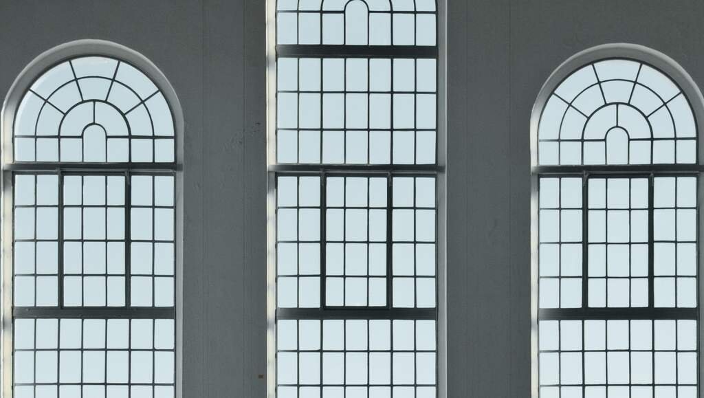 Three tall arched windows of the bath hall, their iron glazing bars against a pale sky over the water.