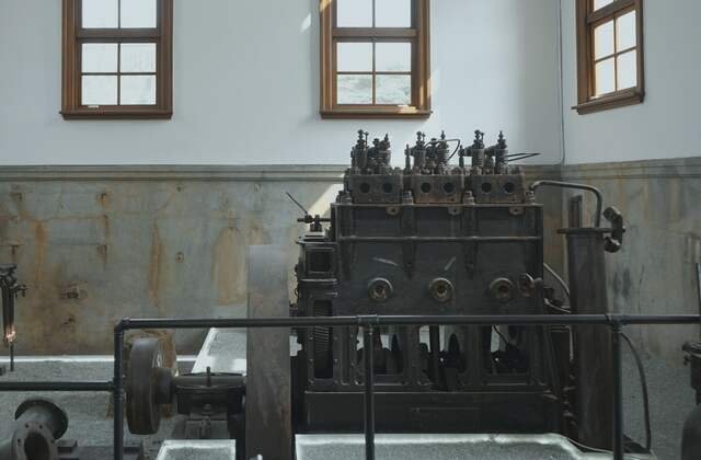An old pumping engine of dark cast iron standing in a whitewashed hall under tall timber windows.