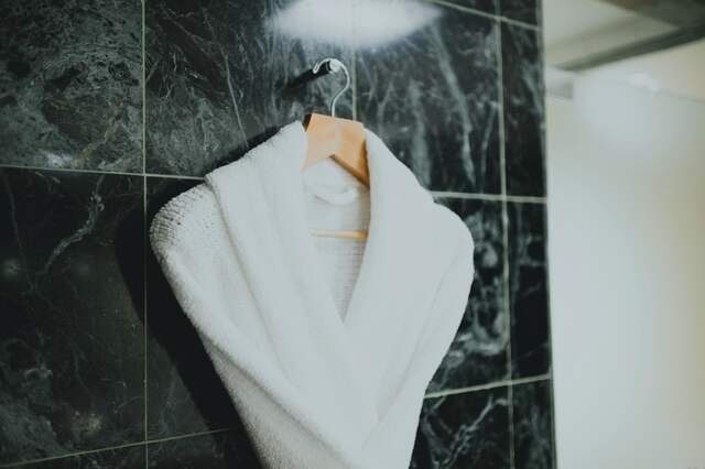 A white towelling robe on a wooden hanger against green-black stone.