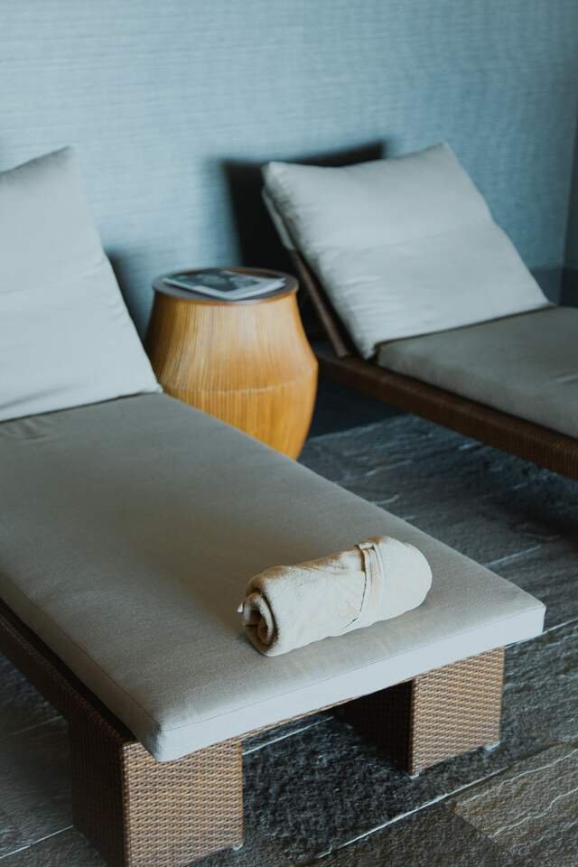 Two low loungers in the quiet hall on a slate floor, a rolled towel waiting on each.
