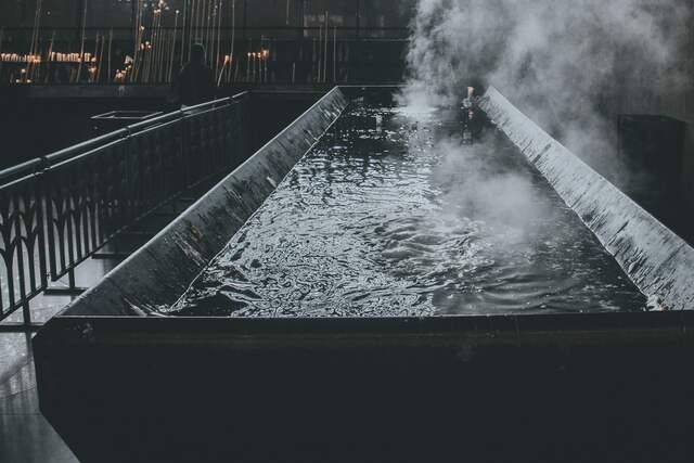Steam rising from a long dark stone trough of water in a dim room.