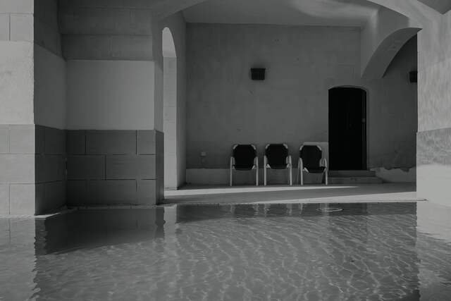 The thermal bath in the old engine pit: still water under stone vaults, three chairs by an arched door at the far end.