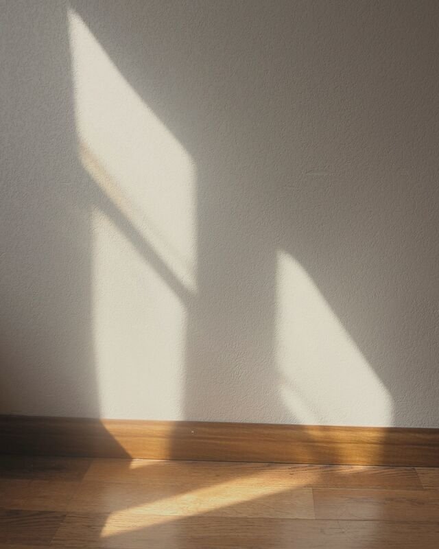 Afternoon sun throwing the shape of a window across a plain plaster wall and the oak skirting below.