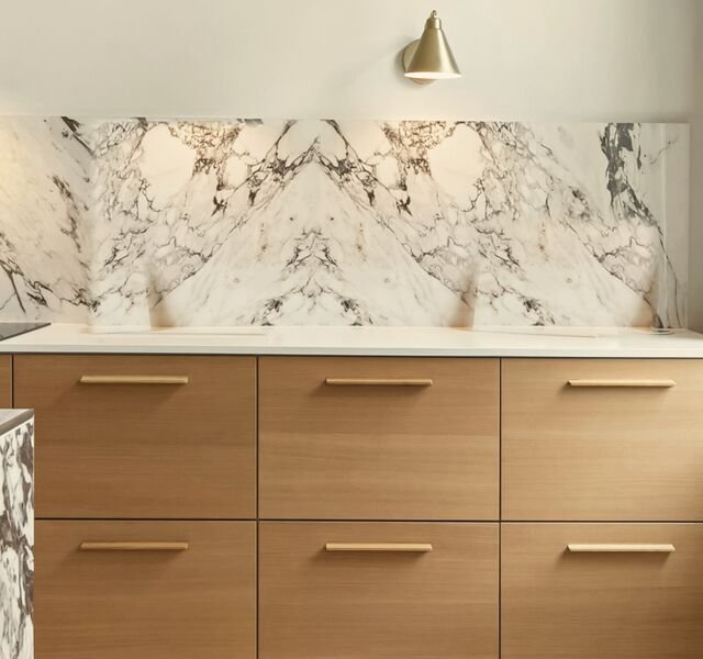The kitchen of Residence 2.04: a run of oak drawers with brass pulls, a book-matched marble splashback under a brass wall light, the original plaster cornice above and a herringbone oak floor.