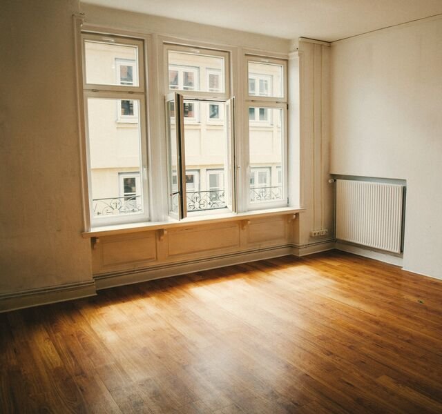Residence 3.02 finished: an empty living room with three windows, a radiator under plain walls and warm light on the oak floor.