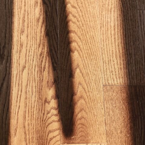 Oak floorboard grain in raking light, with the dark shadow of a window bar across it.