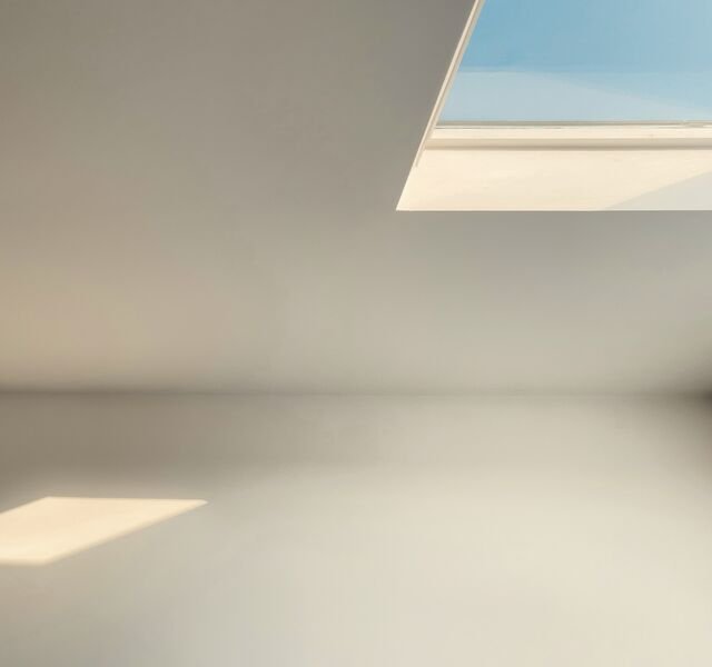 The penthouse stair landing, looking up: plain plaster walls and a square of sky through the roof light.