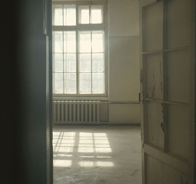 The same floor in March 2024, seen through a half-open door: a stripped room with bare plaster, a cast-iron radiator and window light on the boards.