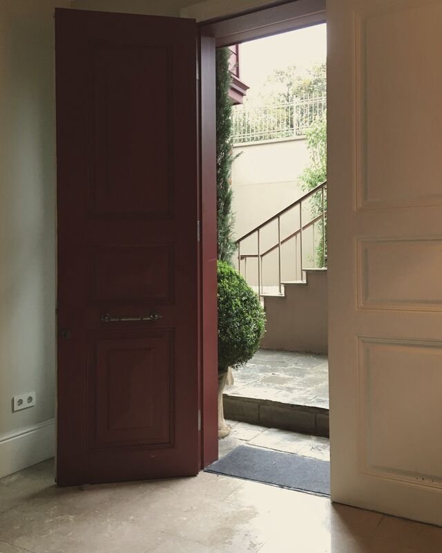 An open panelled front door, deep red, onto stone steps and the light of the square.